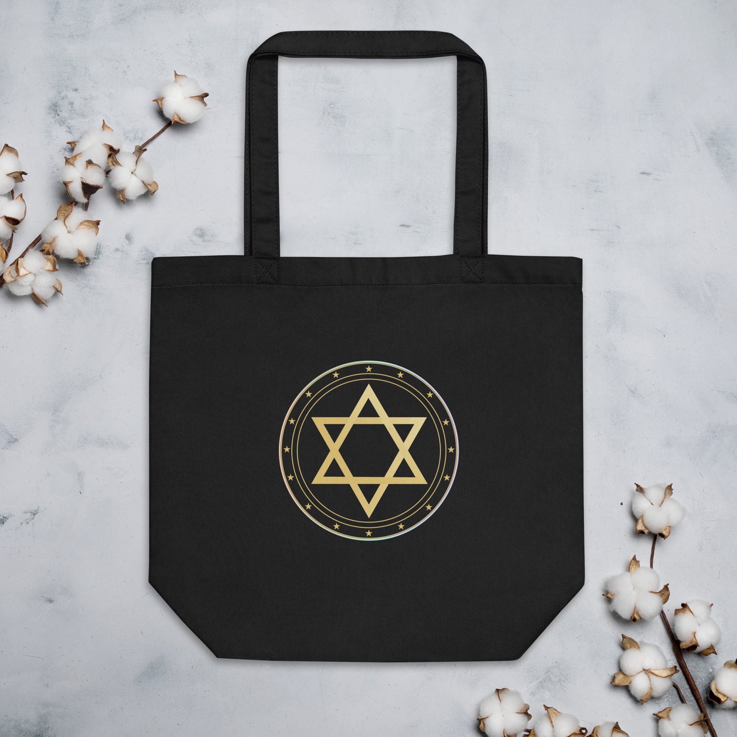 Black tote bag with gold Star of David design on a light gray background with cotton branches.