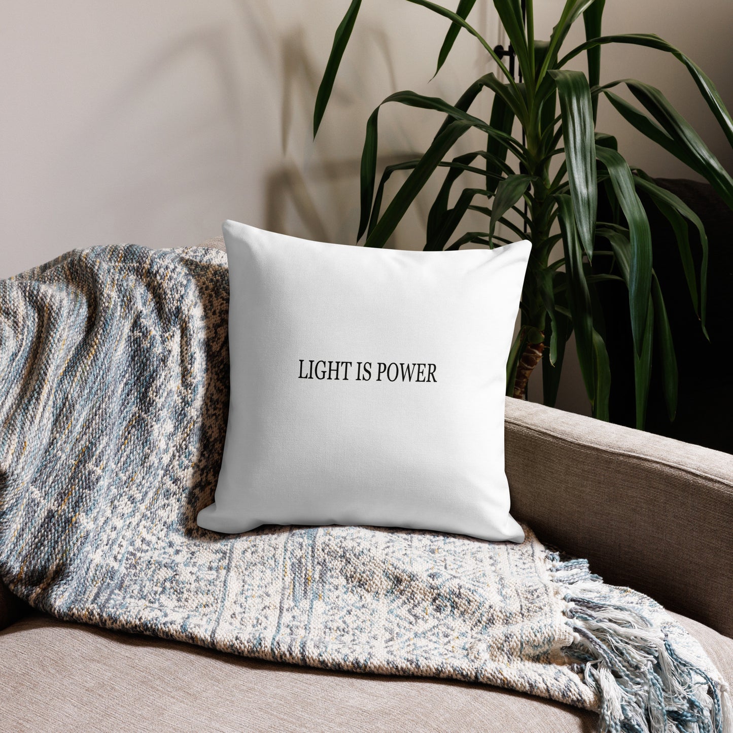 White pillow with 'LIGHT IS POWER' text on a couch with a plant in the background
