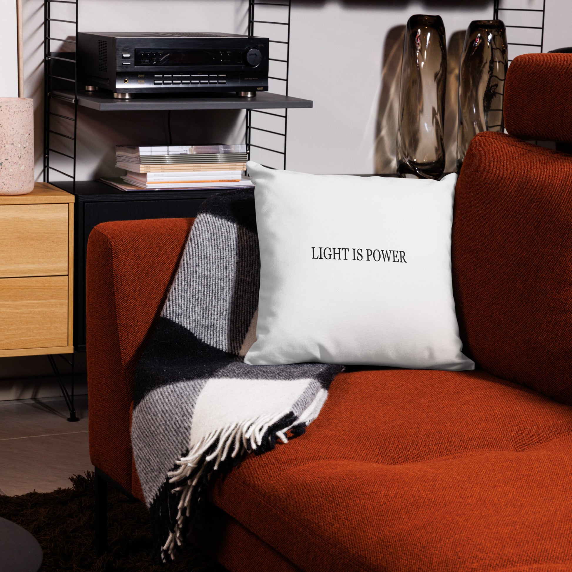 Red couch with a white pillow reading 'LIGHT IS POWER', next to a wooden side table and wall-mounted shelves.