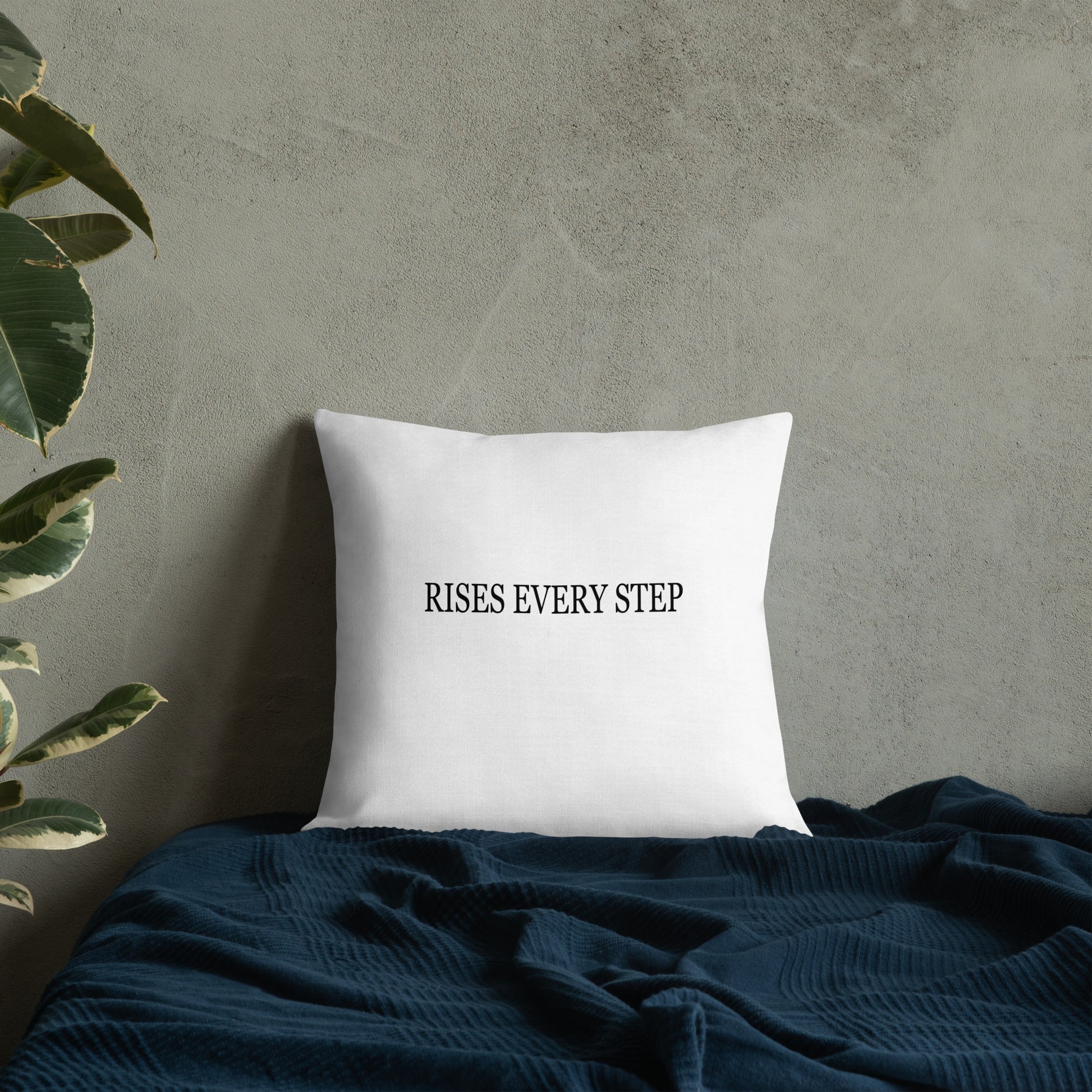 White pillow with text 'RISES EVERY STEP' on a textured wall background