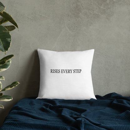 White pillow with text 'RISES EVERY STEP' on a textured wall background