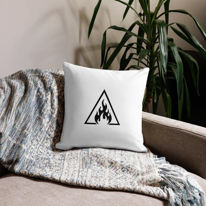 White pillow with a black triangle symbol featuring flames on a couch with a blanket and plant in the background