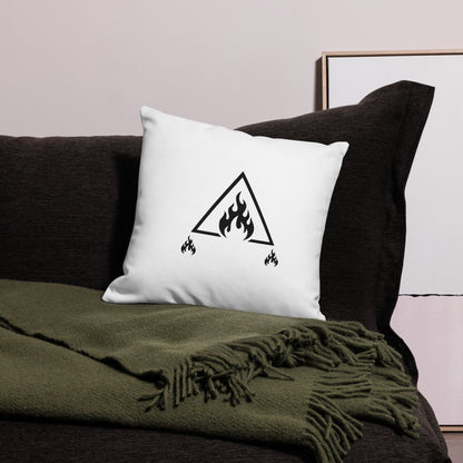 White pillow with a black triangle fire symbol on a dark couch with a green blanket.
