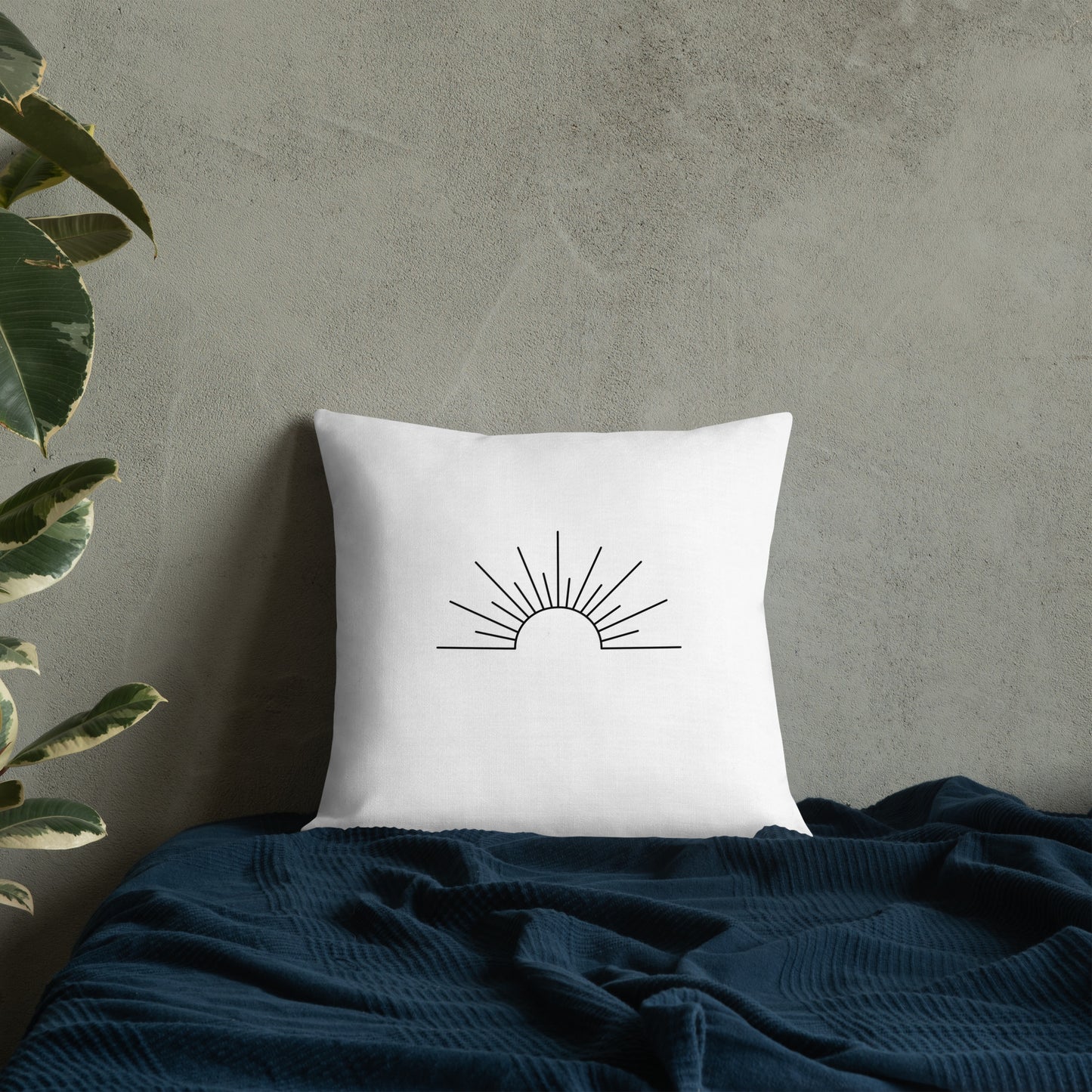 White pillow with sun design on a dark blue blanket against a gray wall.